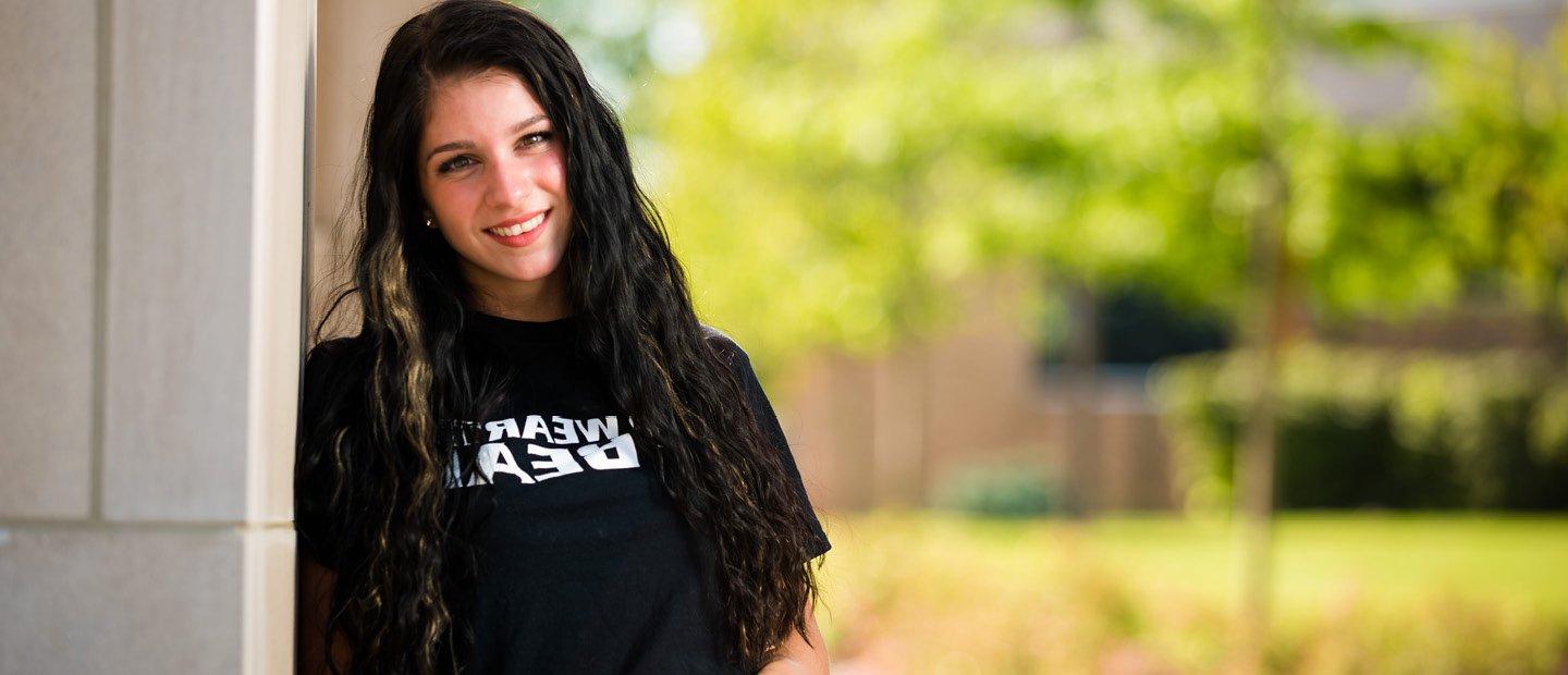 girl in a black t-shirt that ways wear the bear, leaning agains a wall outside